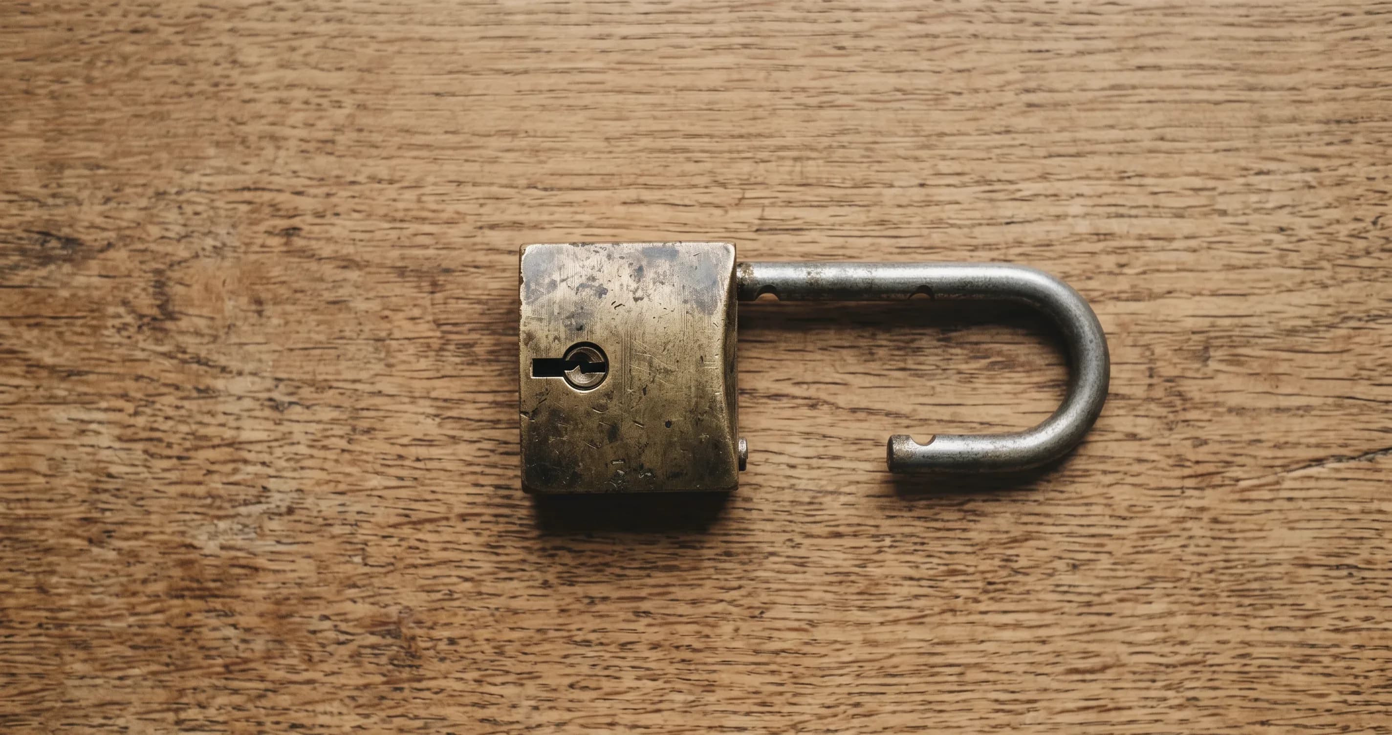 An old brass padlock lying open on a wooden table.