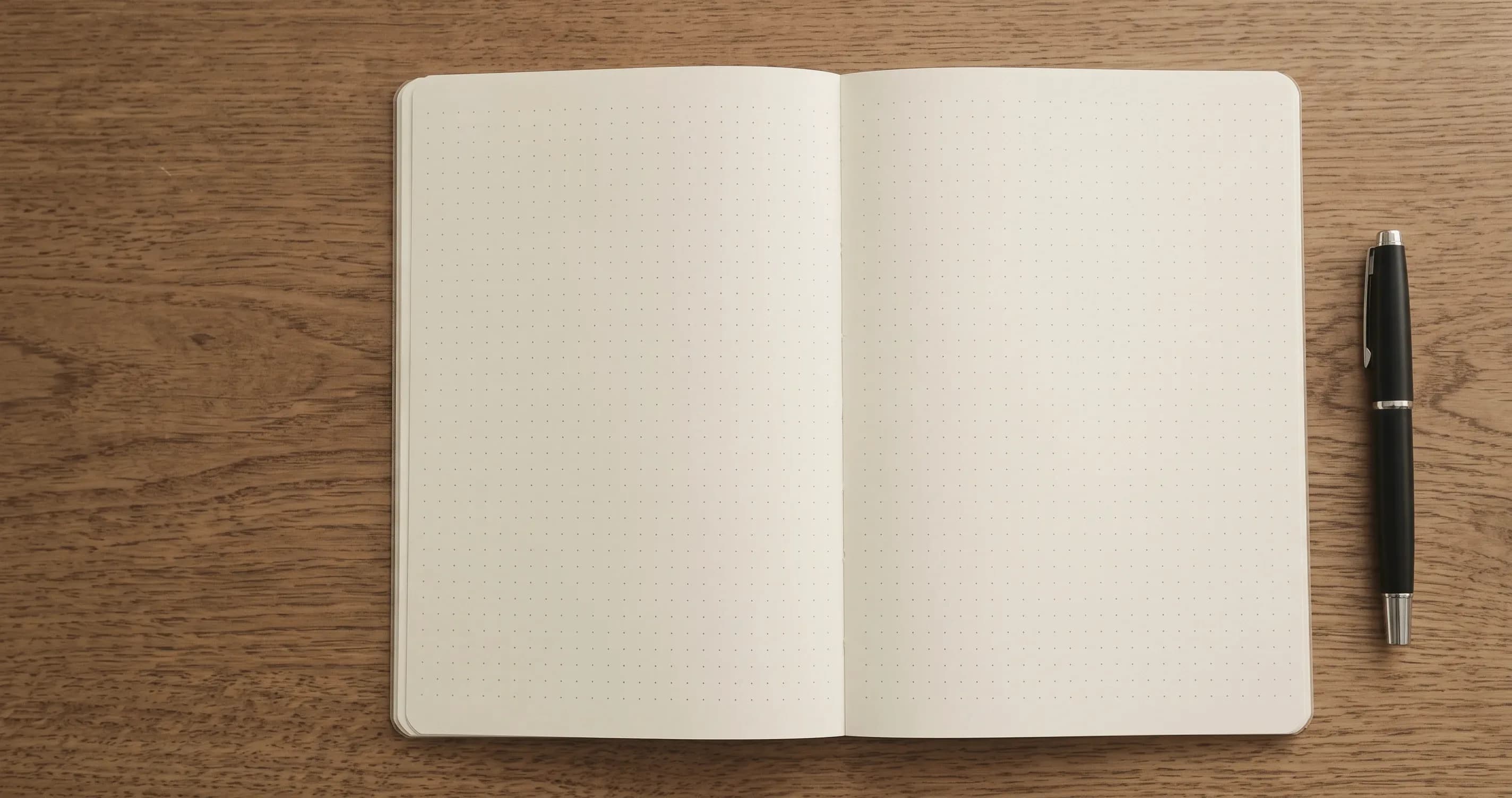 A dotted-grid notebook lying open beside a fountain pen on a wooden desk.