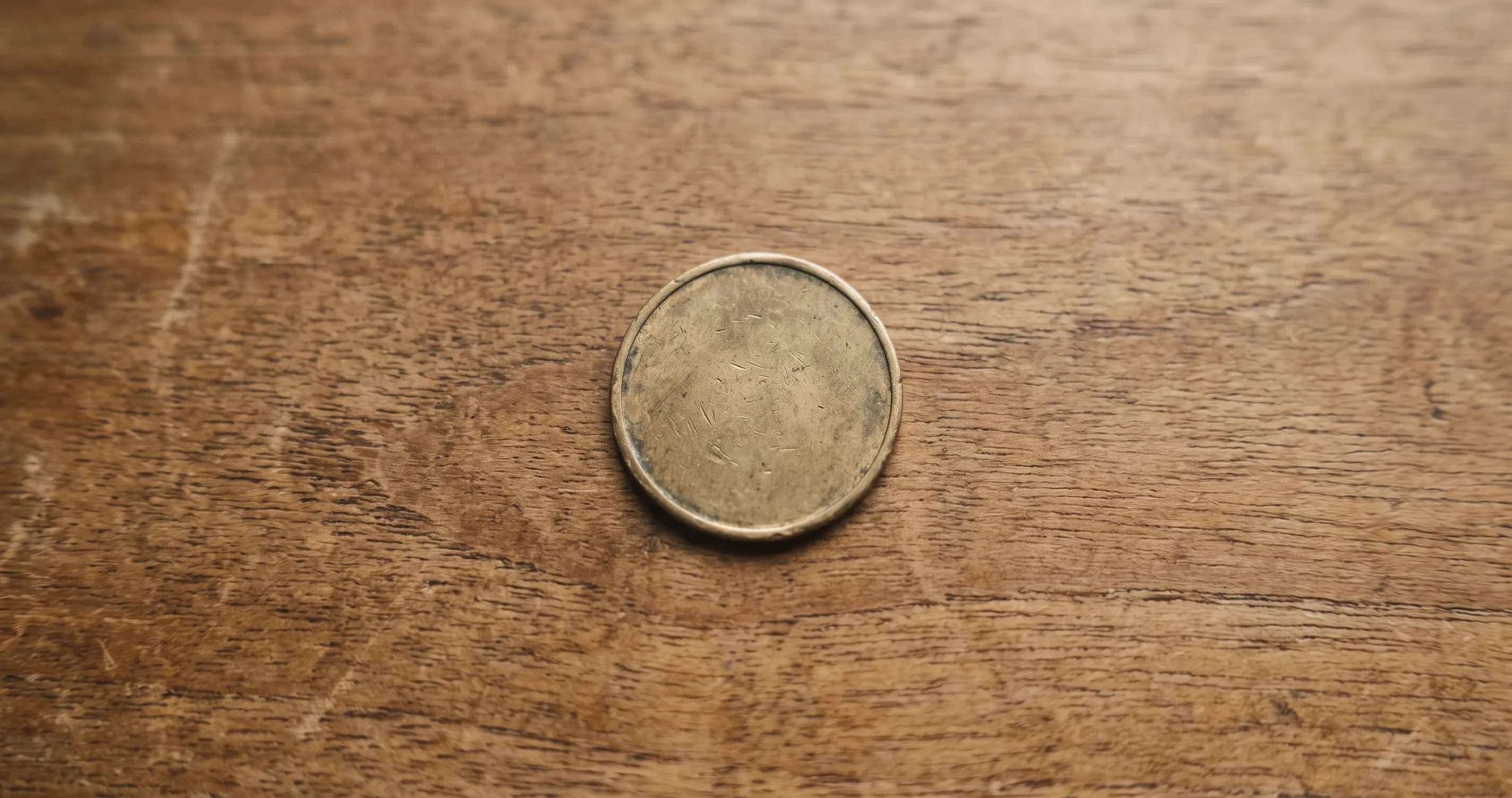 A single arcade token lying on a plain wooden surface.