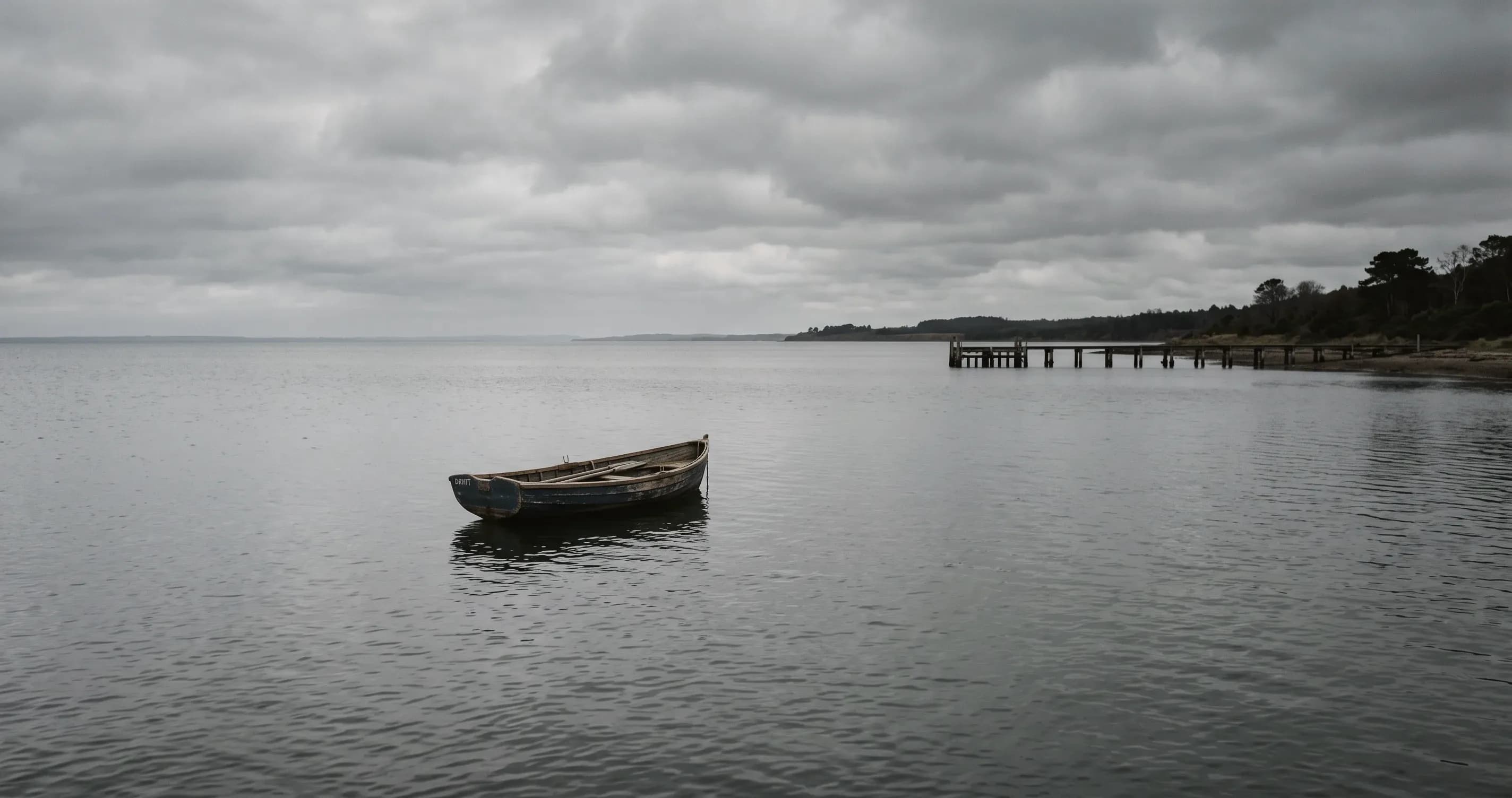 A rowing boat drifting far from a wooden jetty on flat grey water.