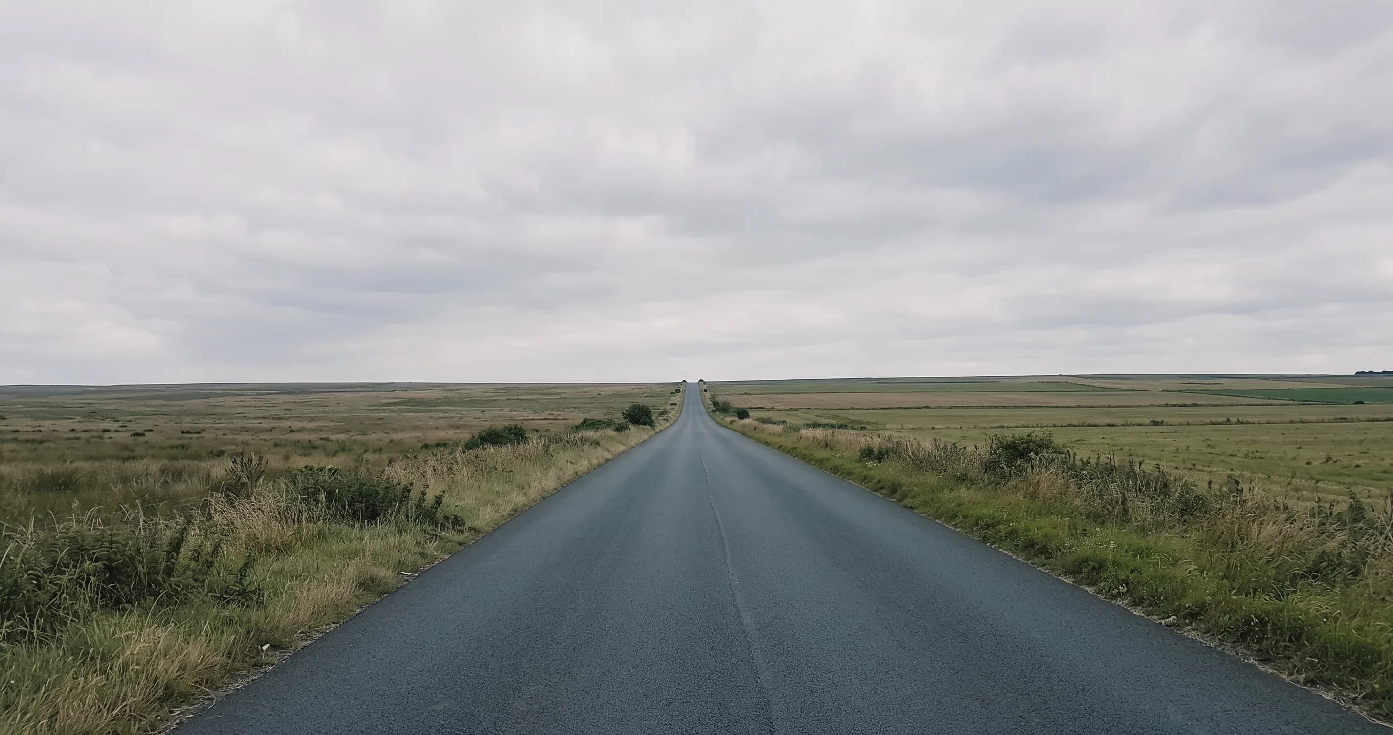A long straight empty road stretching to the horizon across open countryside.
