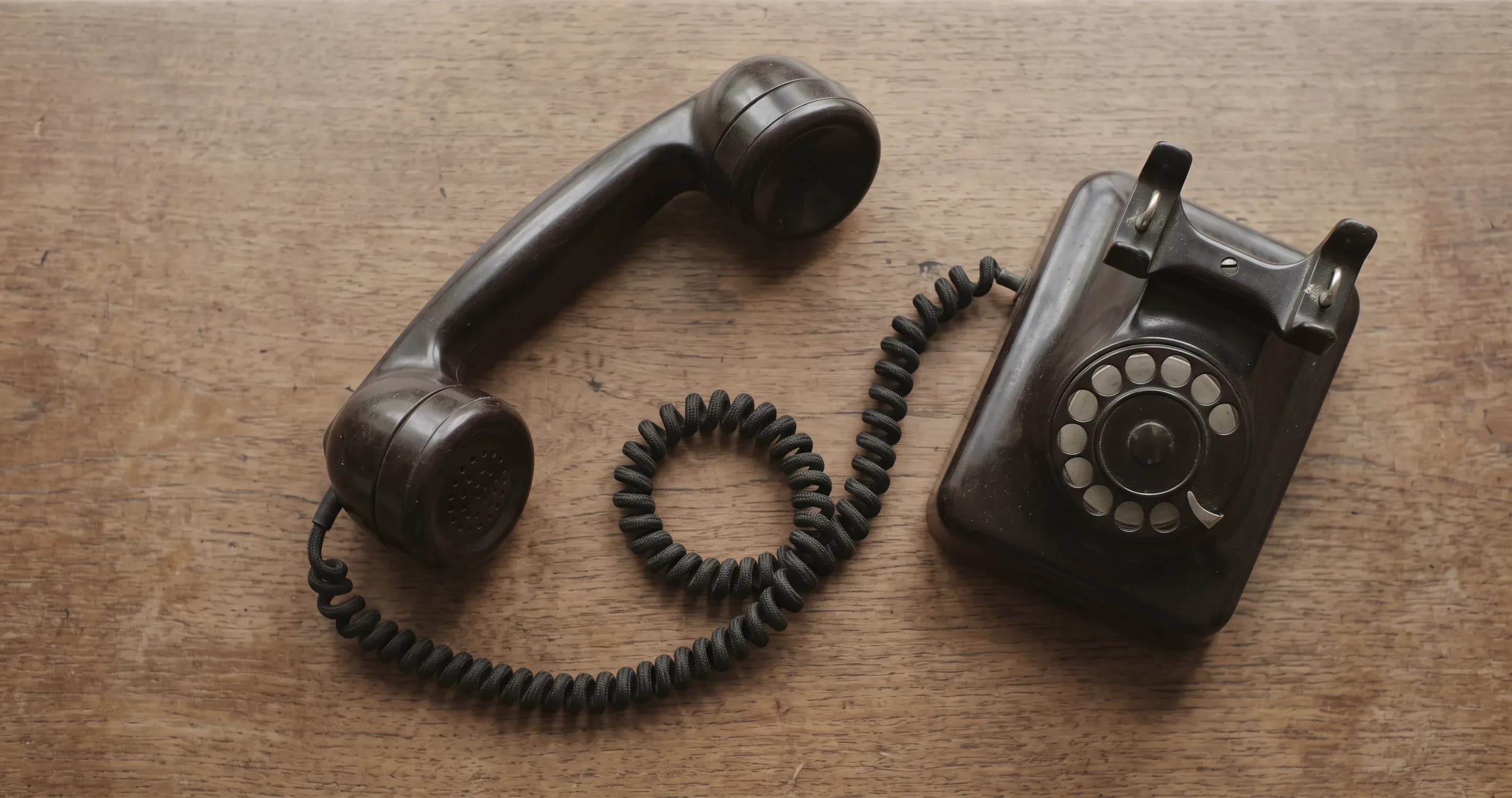 An old telephone handset resting off the hook on a wooden desk.