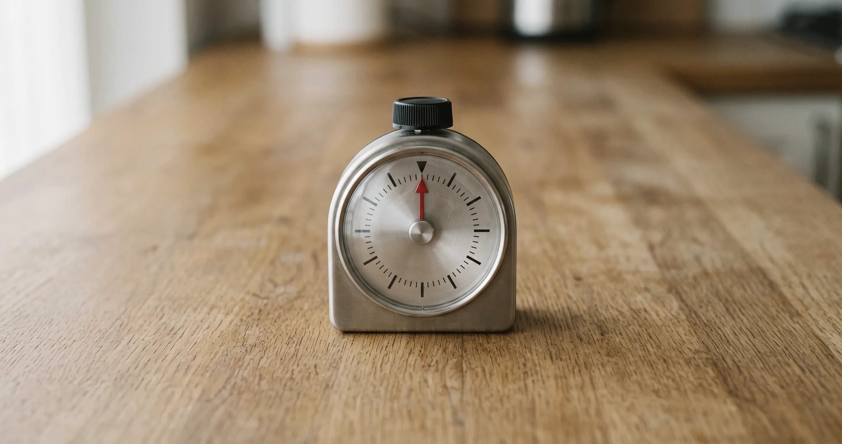 A mechanical kitchen timer standing alone on a plain wooden surface.