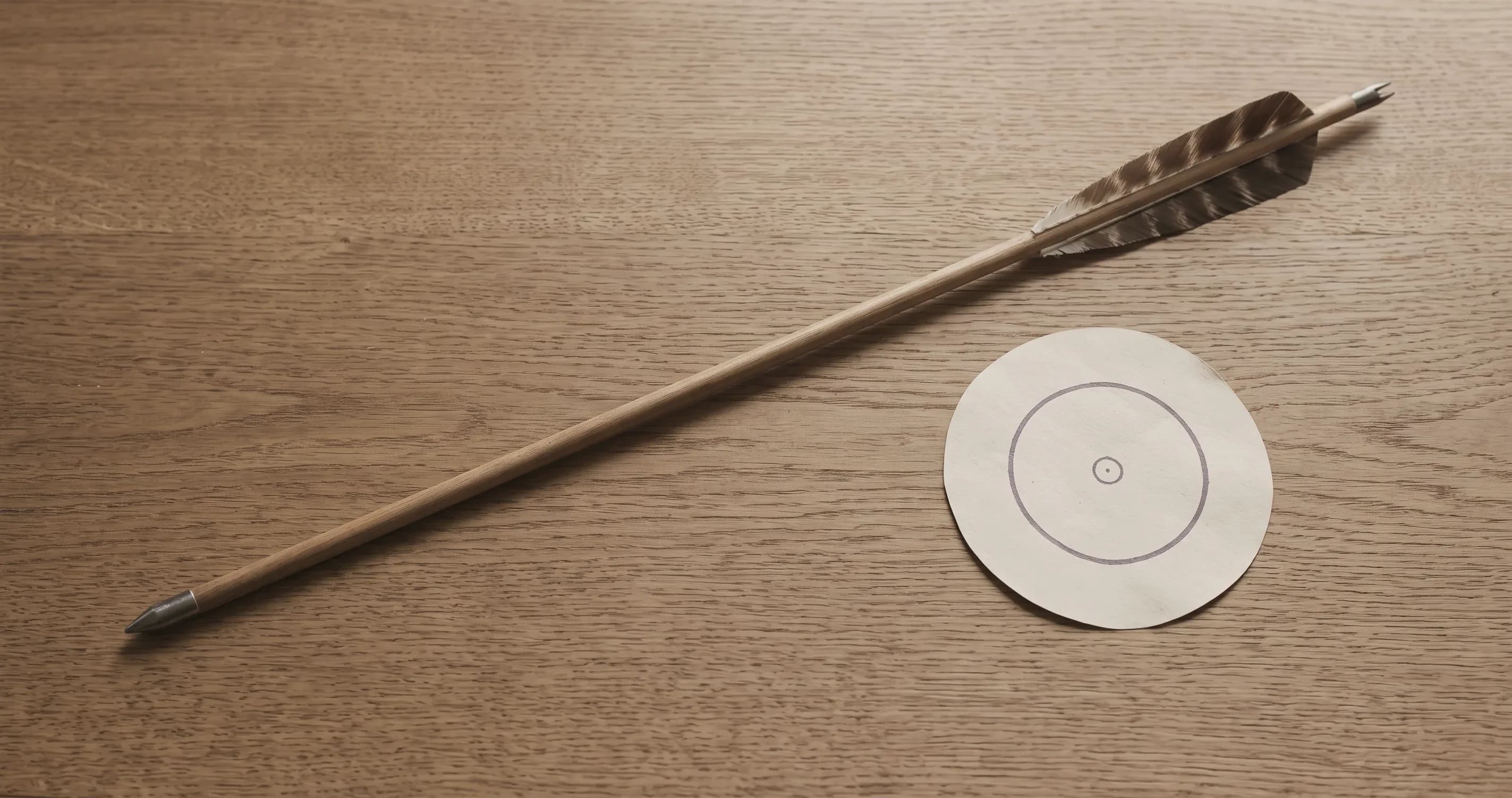 A single arrow lying beside a small target on a plain wooden surface.