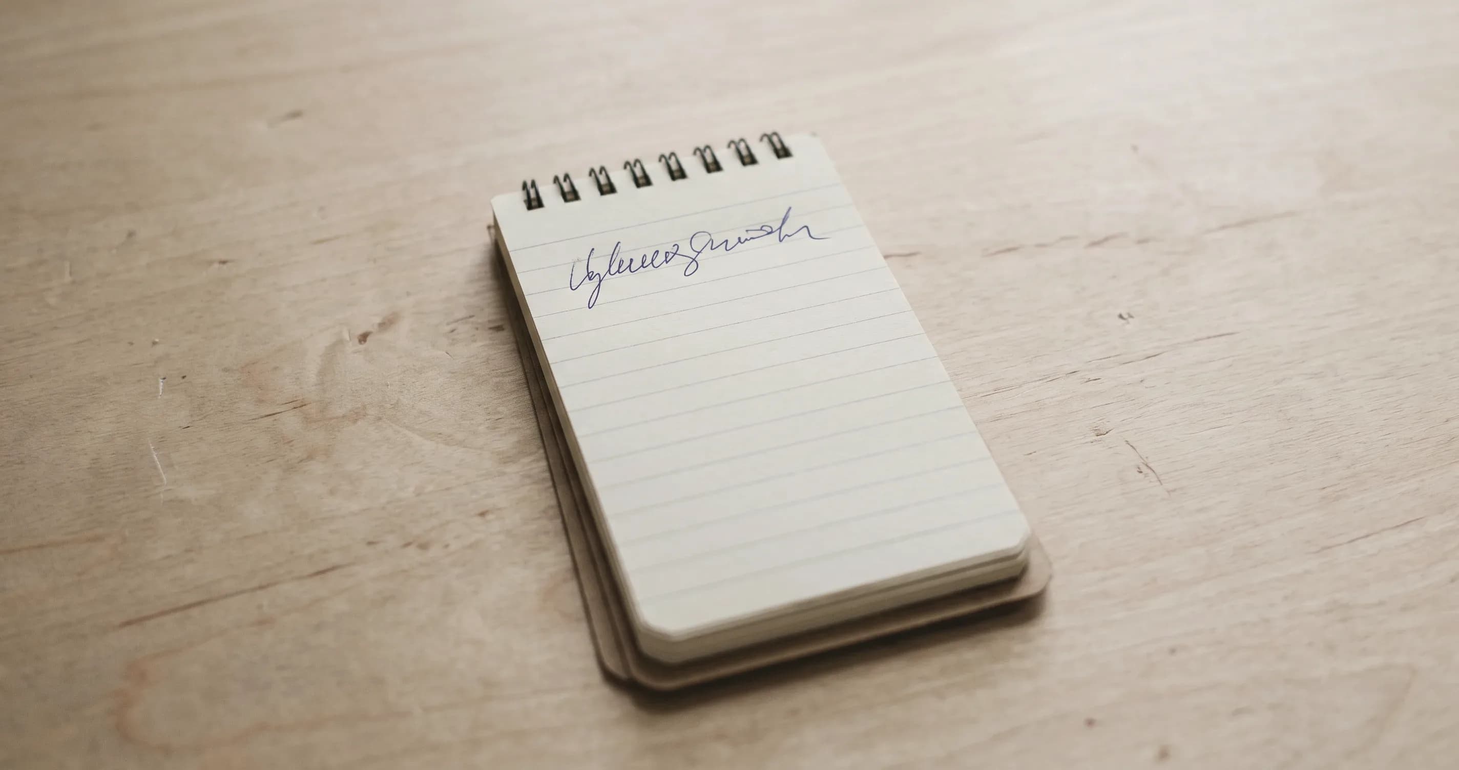 A small notepad on a desk with a single short handwritten line on the top page.