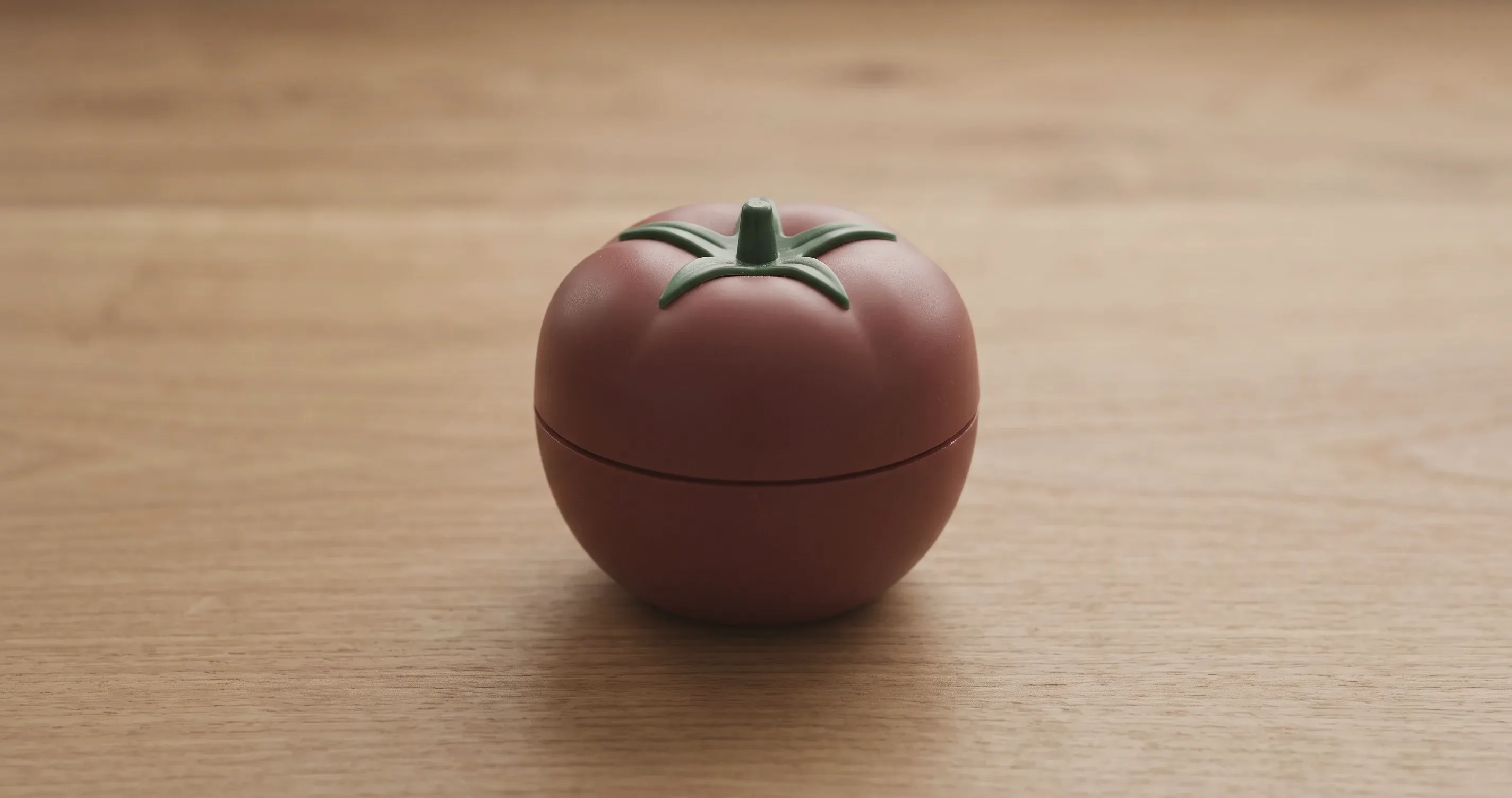 A tomato-shaped mechanical kitchen timer on a plain wooden surface.