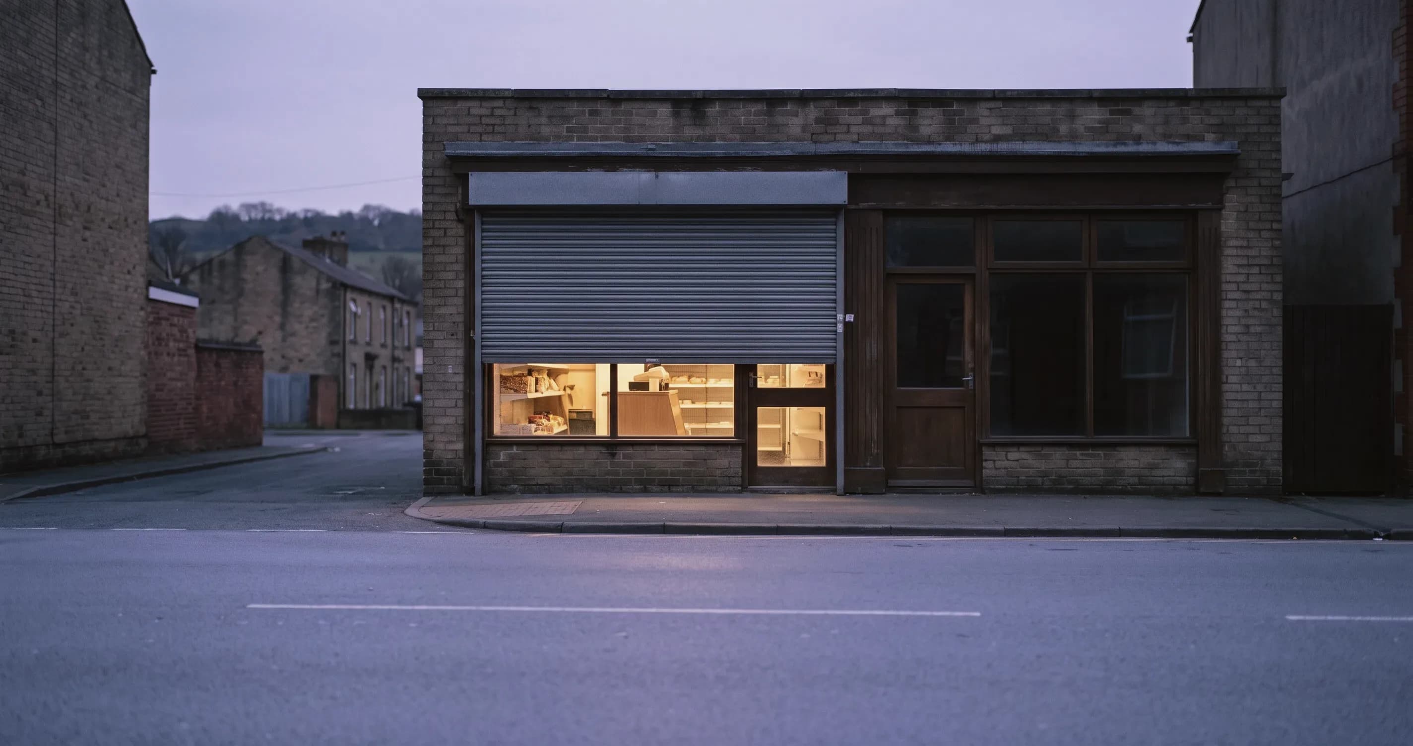A shop with its lights on and shutters half down.