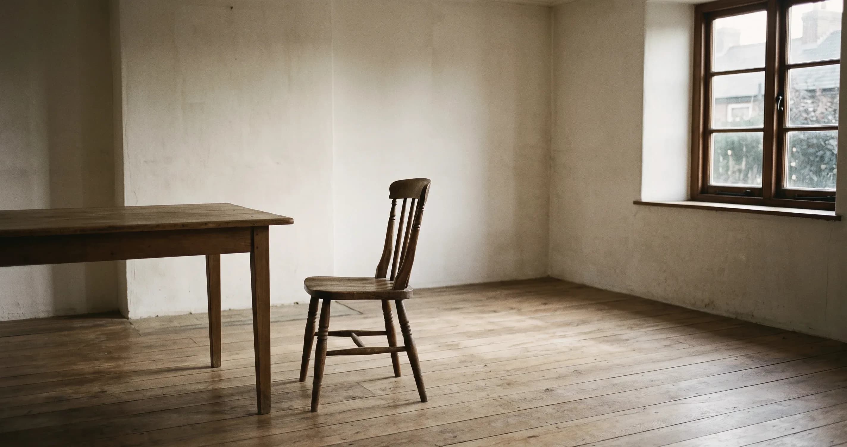 An empty wooden chair pushed back from a cleared table in an otherwise bare room.