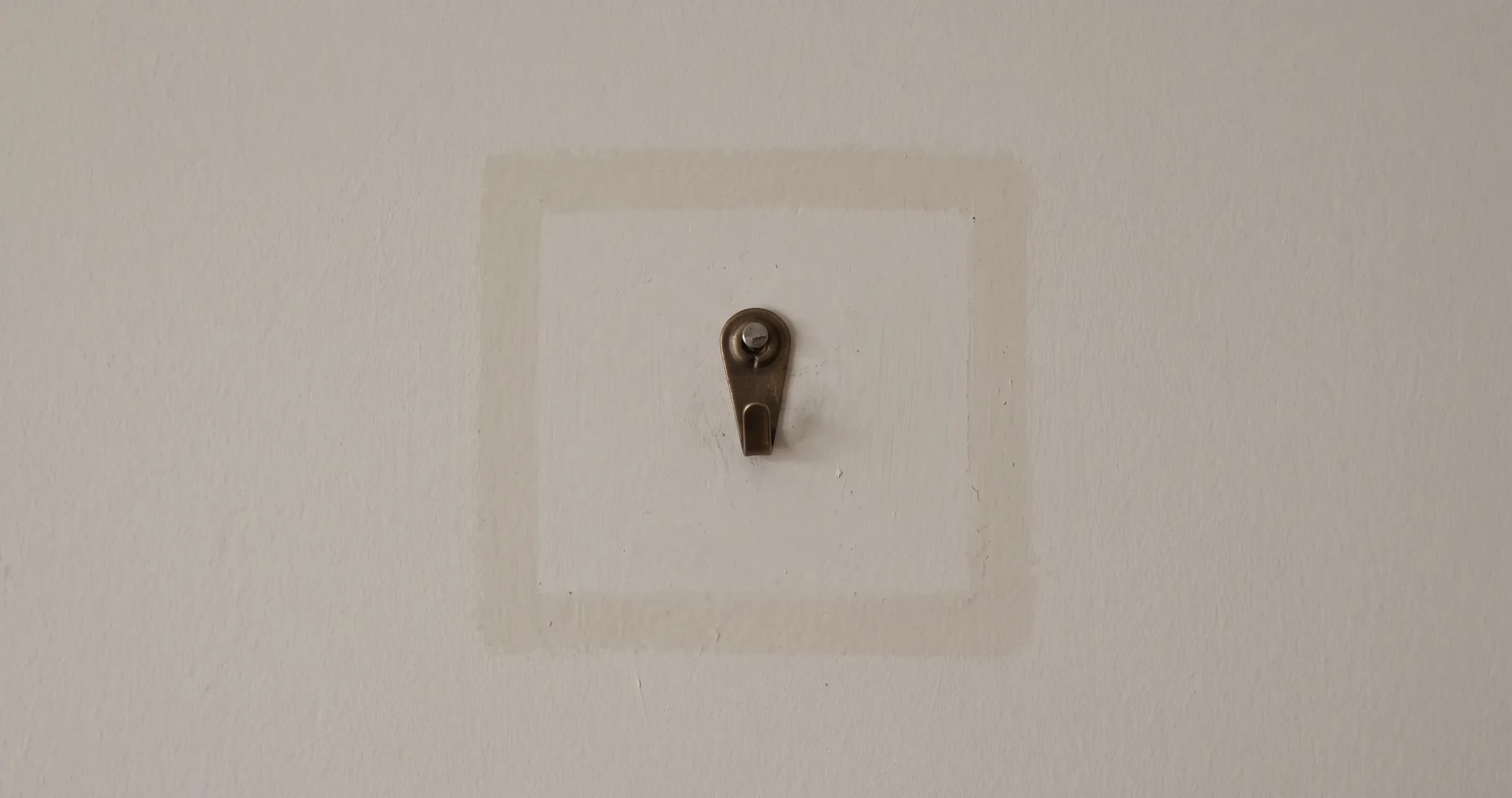 An empty picture hook on a plain wall, with a faint mark where something hung.