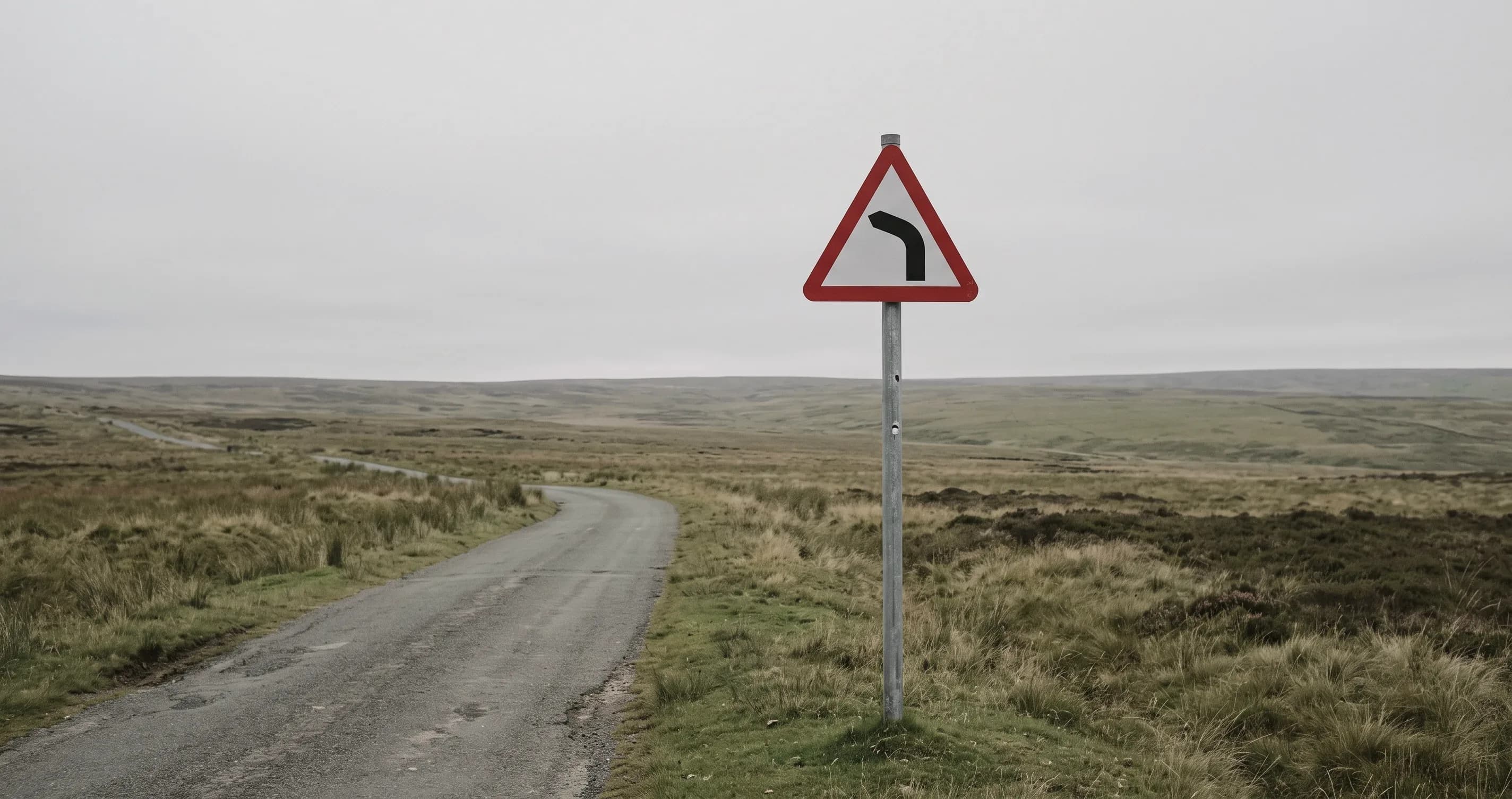 A road sign showing a bend ahead, standing in open countryside.