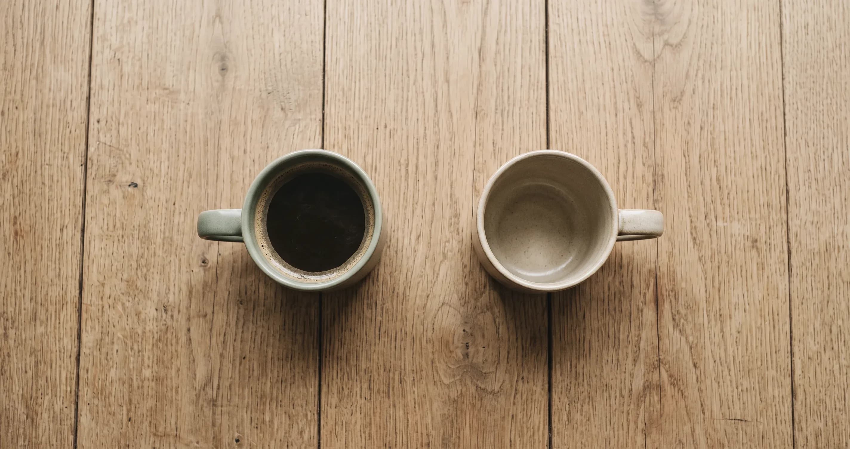 Two mugs on a table, one full and one empty.