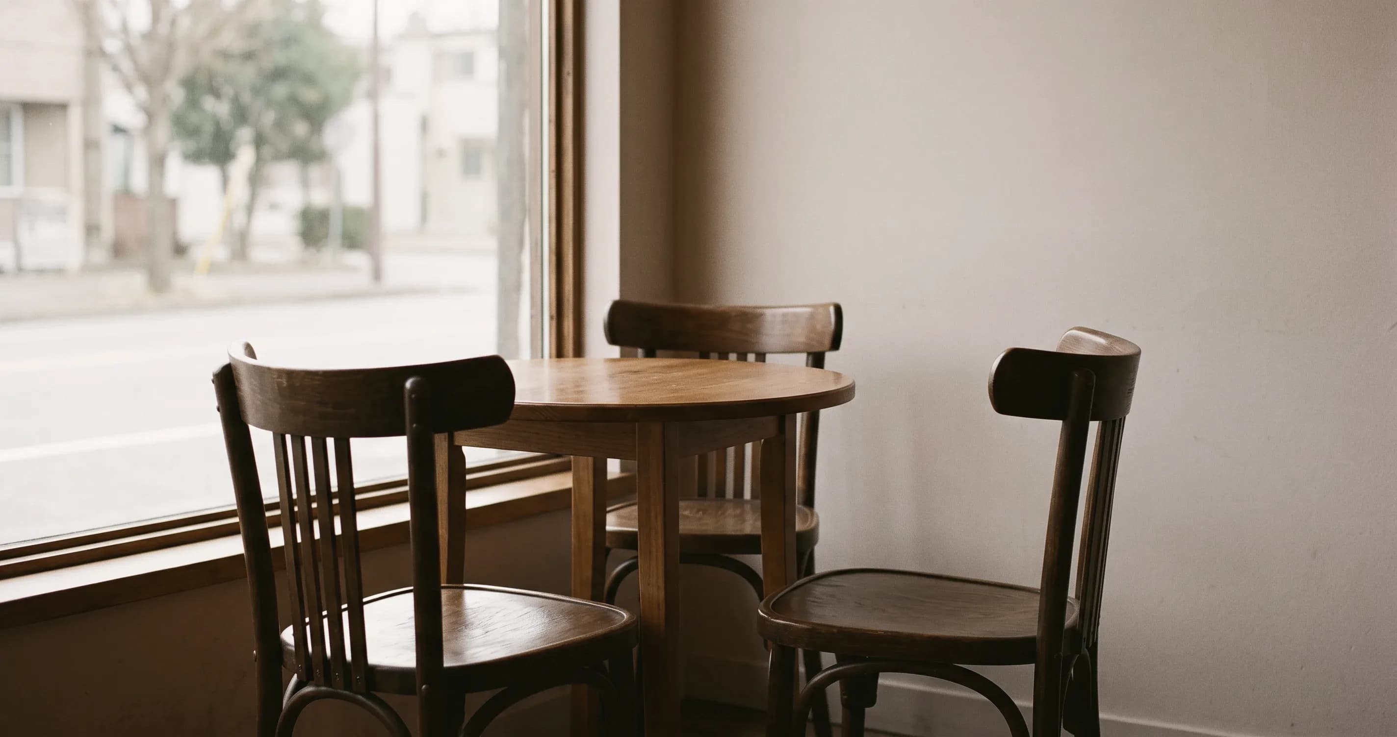 Empty chairs around a small table by a café window.