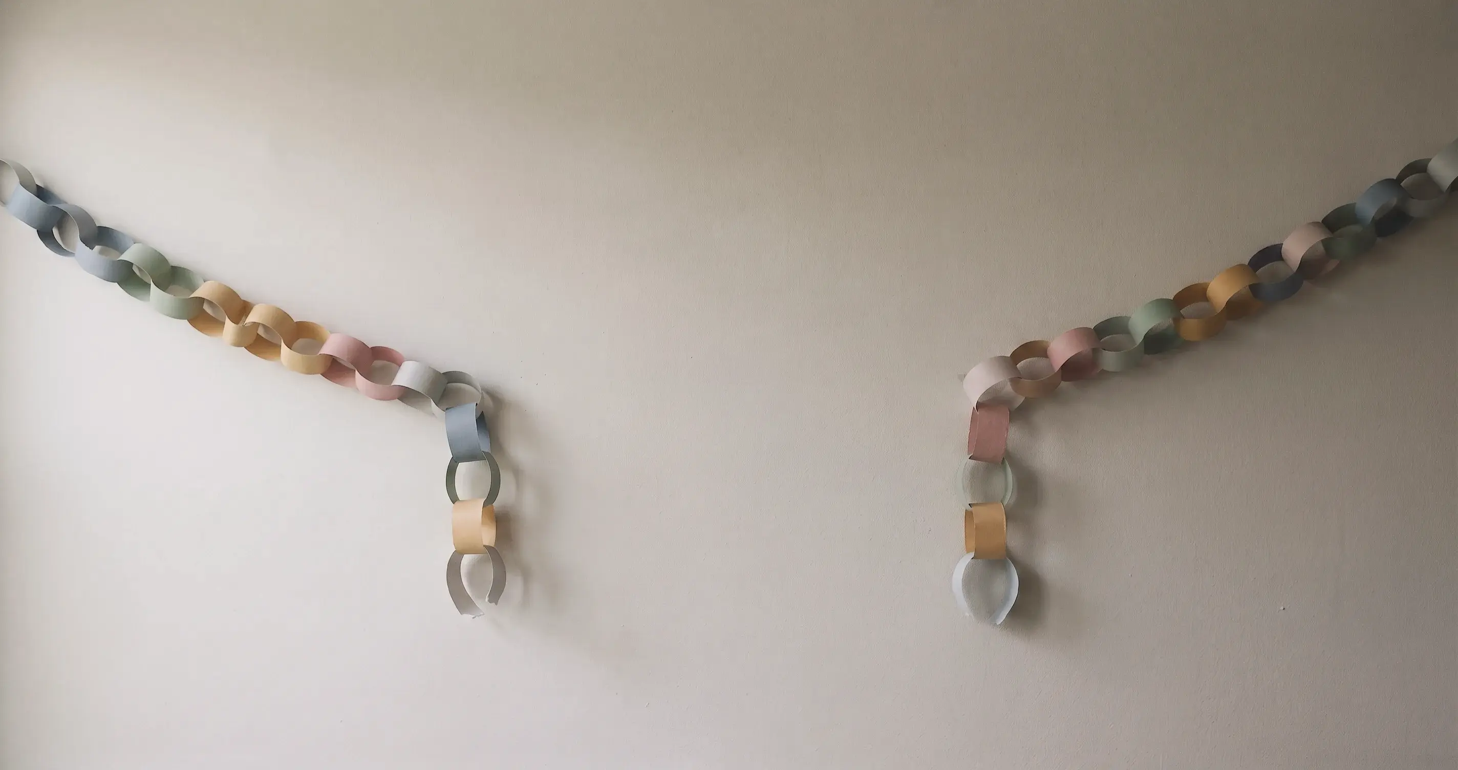 A paper chain strung across a plain wall, torn through in the middle, the two severed ends hanging down.