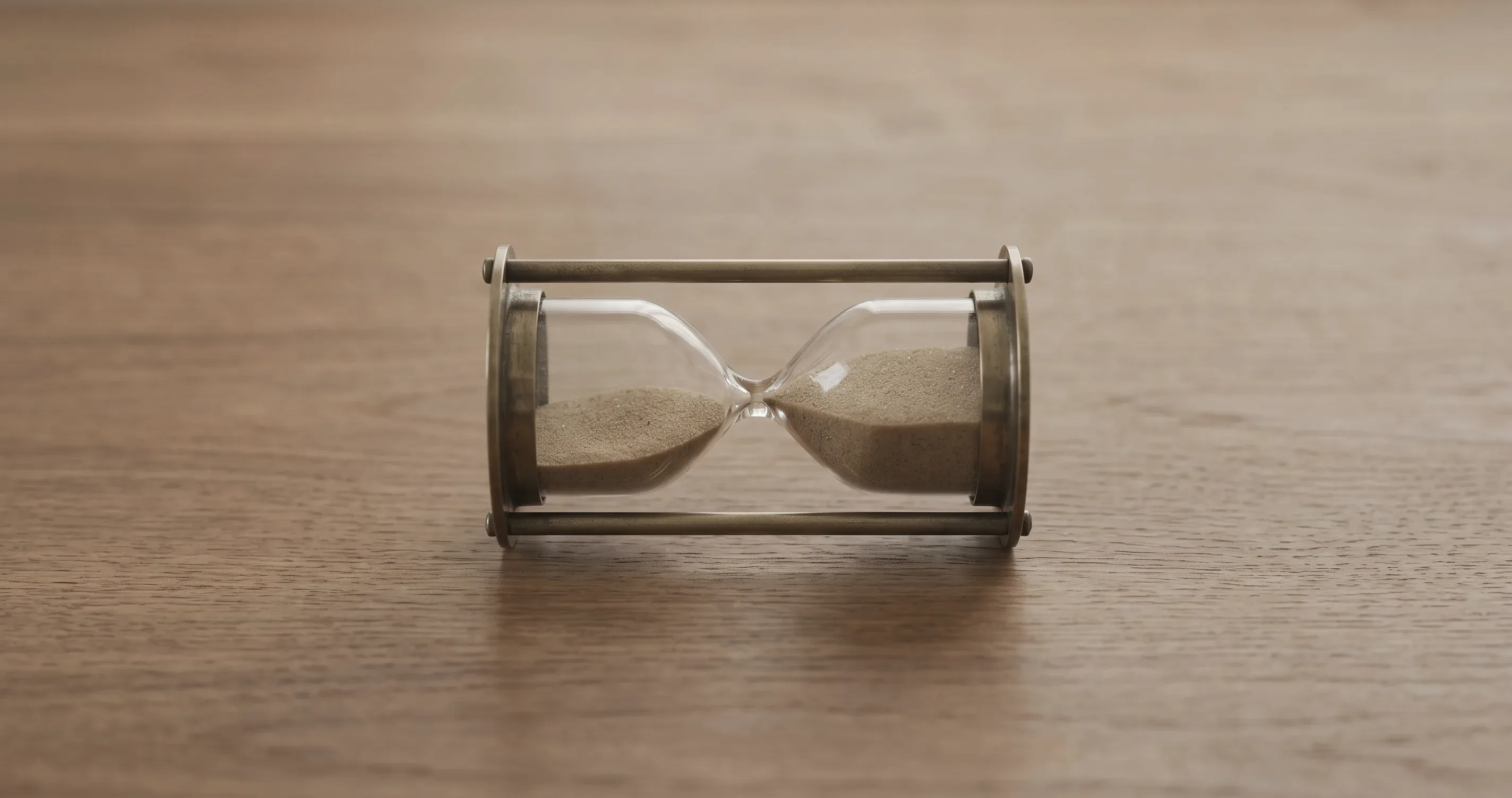 A small hourglass lying on its side on a plain wooden surface.