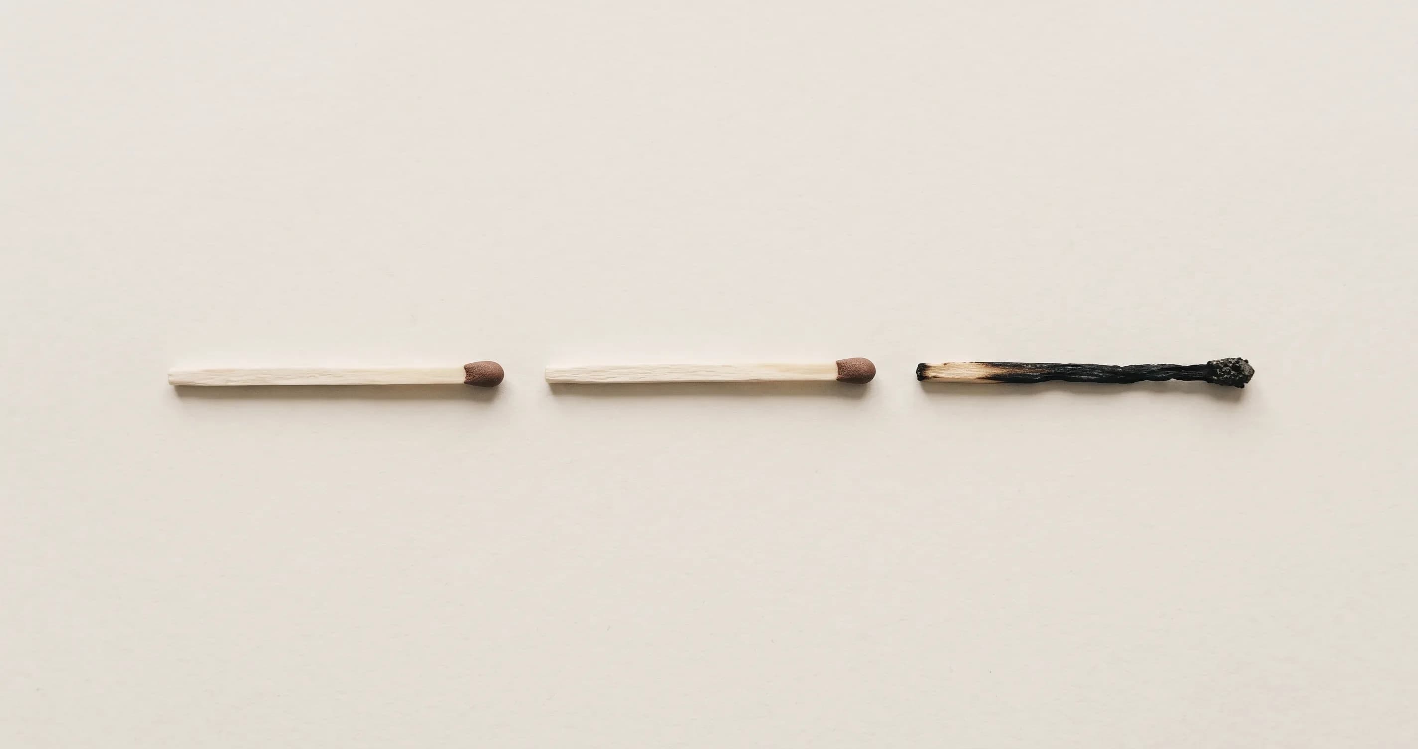Three matches lying in a row on a plain surface, the third one burnt out.