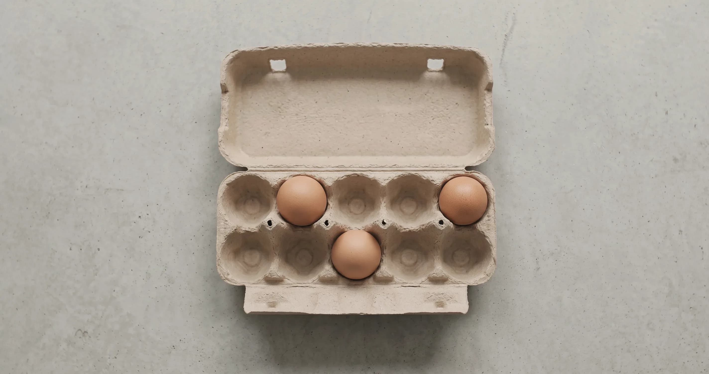 Three eggs in a large cardboard egg box built for a dozen, the other spaces empty.