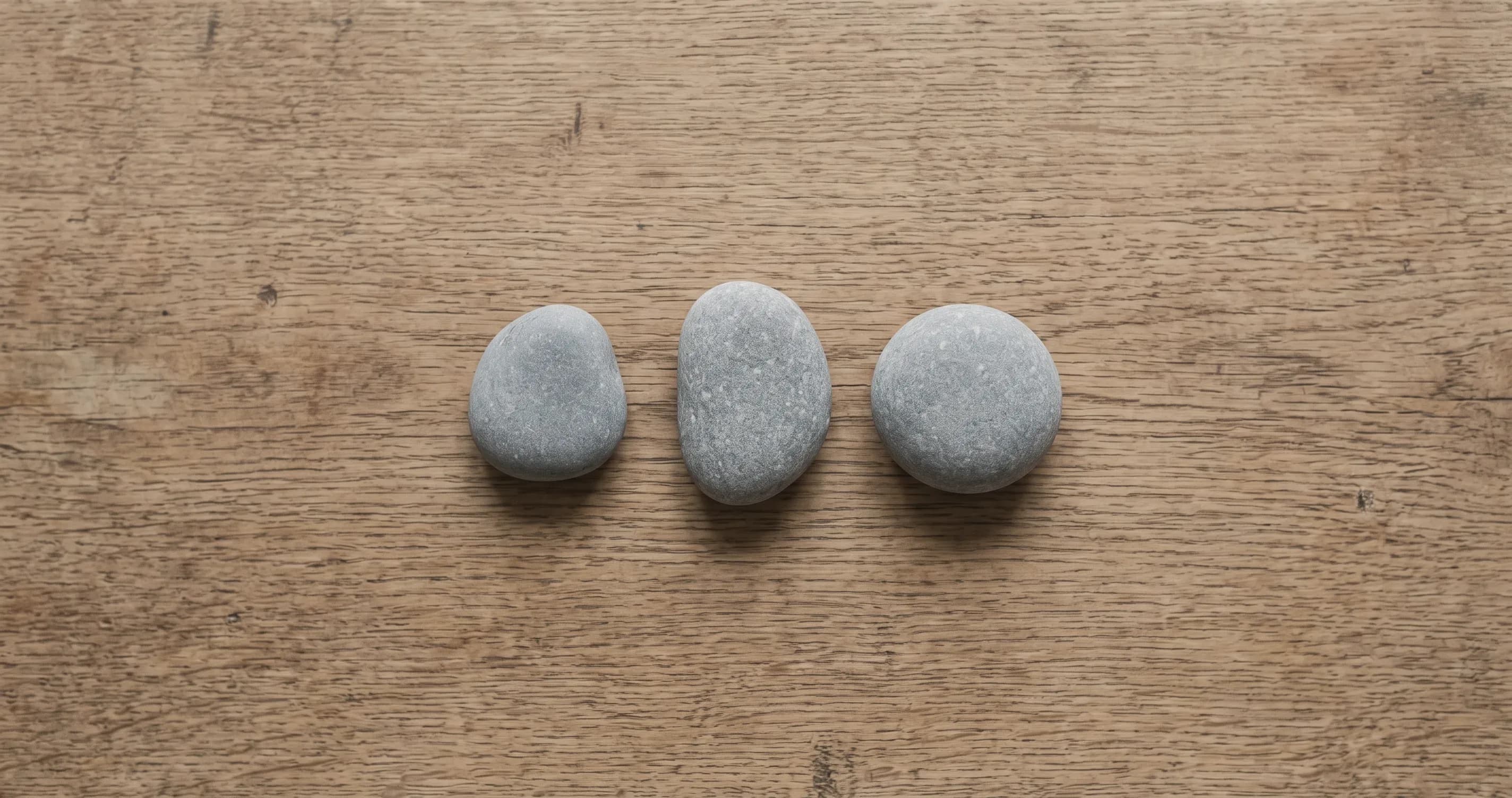Three small stones lined up on a plain wooden surface.
