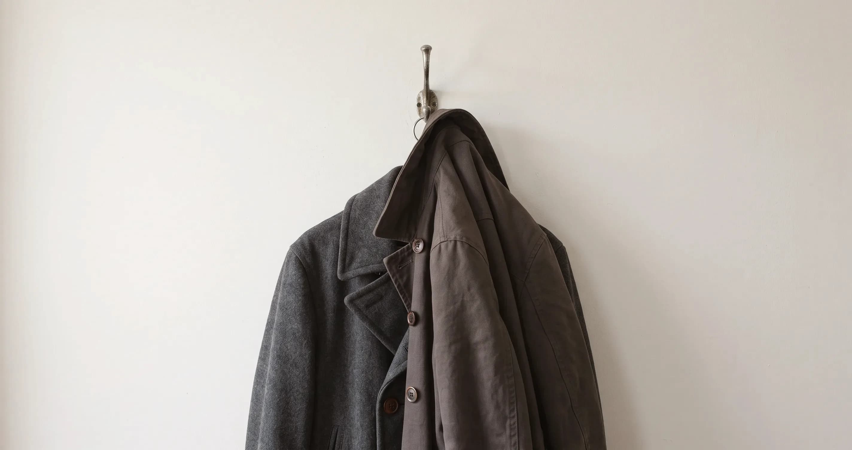 Two coats hanging on a single hook, one over the other.