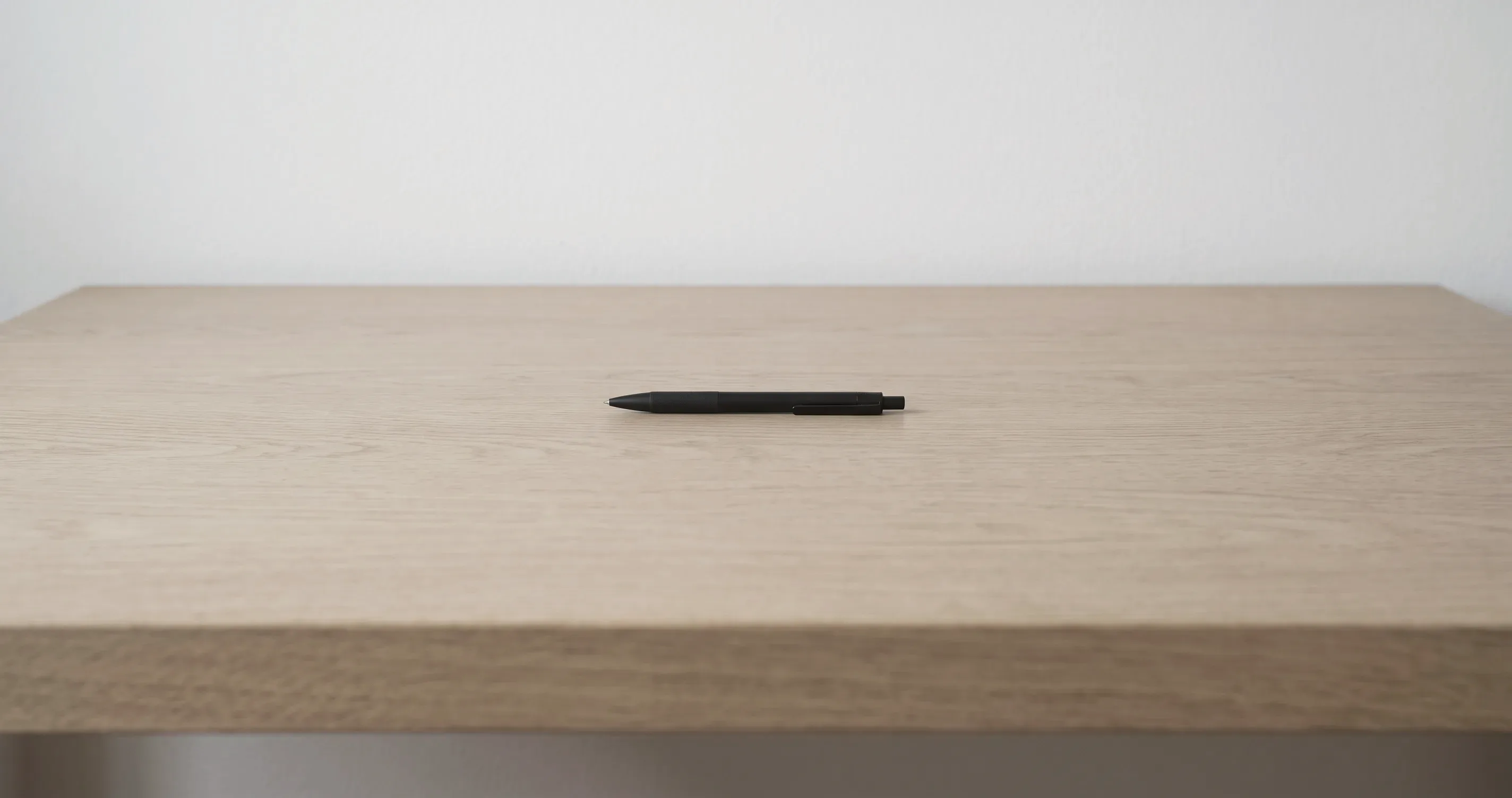 A wide bare desk with a single pen lying at the centre and nothing else on it.