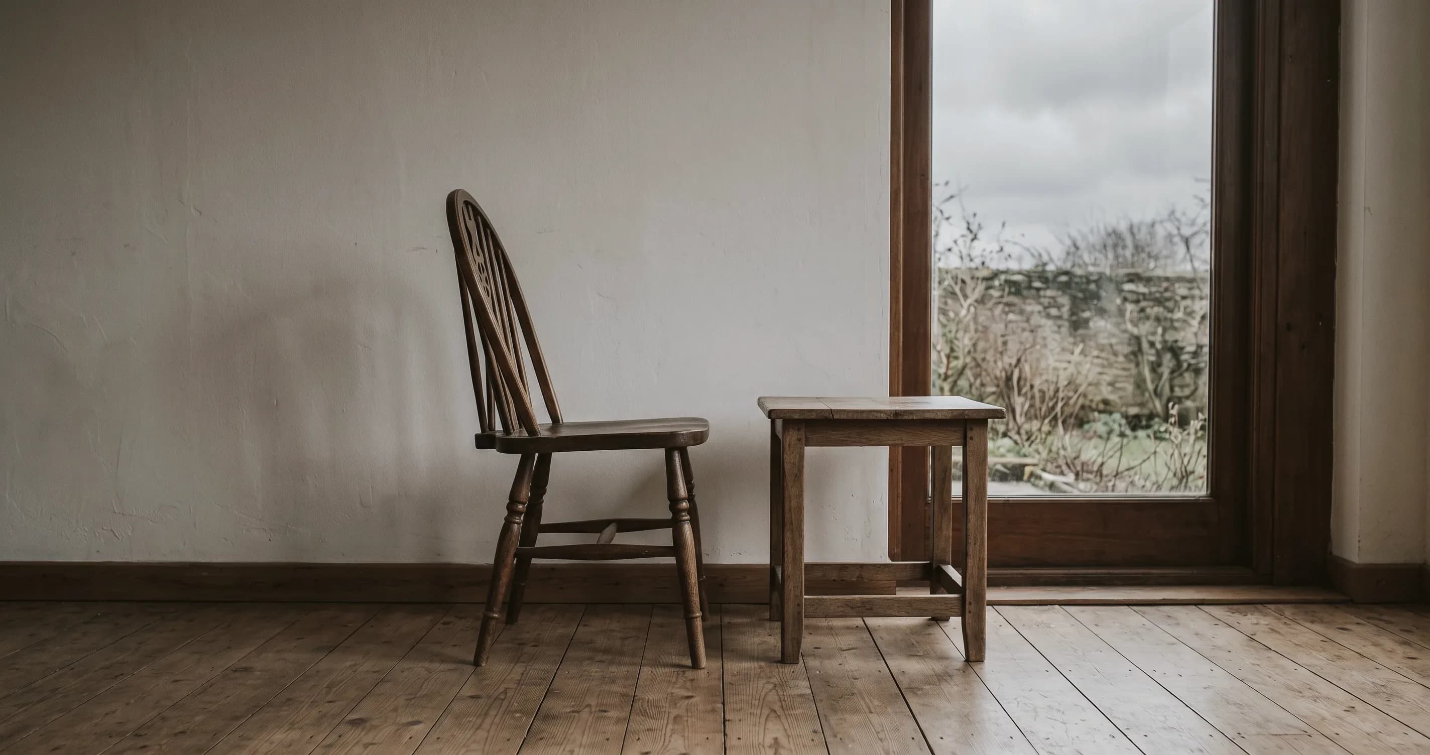 An empty chair beside a small table by a window on a grey afternoon.