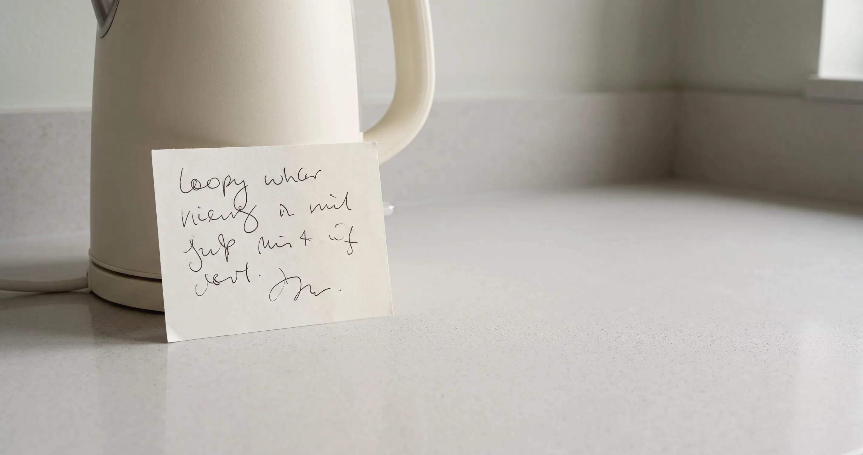 A handwritten note left propped against a kettle on a kitchen worktop.